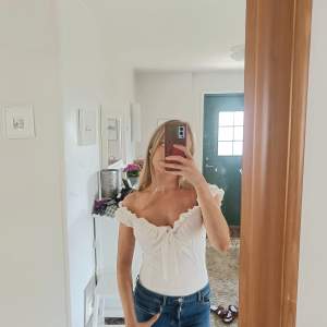 Vit body suit med off shoulder ärmar med en knut detalj där fram