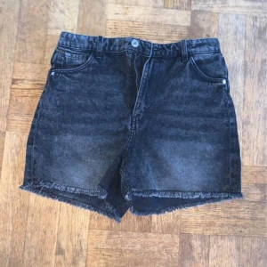 Svarta jeansshorts - Ett par svarta jeansshorts med fransiga kanter. Shortsen har en knapp och dragkedja framtill samt två framfickor och två bakfickor.