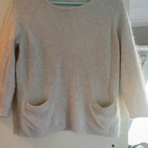 Stickad tröja med trekvartsärm - Vit stickad tröja med trekvartsärm och dekorativa påsydda fickor på framsidan. Tröjan är i fint skick och strl m, sitter perfekt överskred på mig som vanligtvis är en s i tröjor. Från märket superdry och fin materialsammansättning🥰