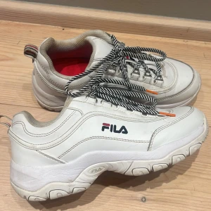 Äkta Fila skor - Äkta Fila skor. Vita med randiga snören o röd innersula. Använda men bra skick. Säljer p.g.a användes för länge sedan. Ska försöka rengöra de så att de blir lite vitare. Storlek 38 men passar oxå mig med 39. Nypris ca 500-800. KOLLA MIN PROFIL💕
