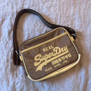 Superdry crossbody väska - Snygg brun superdry crossbody/axelväska i bra skick. Går att justera längd på rem 