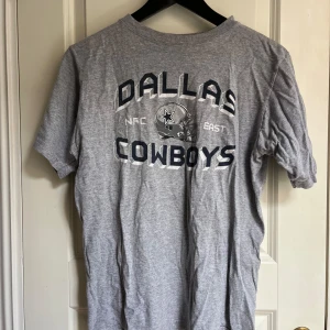 Grå t-shirt - En grå t-shirt med tryck av Dallas Cowboys. T-shirten har en rund halsringning och korta ärmar.