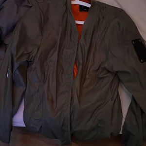 Bomberjacka grön - Grön bomberjacka från Galagowear, med orange insida. Jackan är väldigt tunn så skulle klassa den som sommarjacka. Storlek S (herrmodell) 