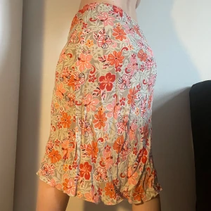 Blommig kjol i beige och rött - Midikjol i beige med mönster av blommor i rött, orange och rosa. Passar mig som har s och är 165 cm. Kan mötas på söder eller posta. Skriv helst innan ni trycker köp nu då jag är borta en del i sommar. 