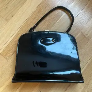 Vintage svart högblank handväska. Snygg metallknäppning i guldig färg. Lite smårepor men inget som stör. Väskan är ca 22x25x7 + handtag. 