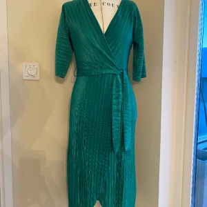 Omlottklänning grön, stl xs - Tunn och skön omlottklänning i skönt material. Behöver aldrig strykas. Fint använt skick, sommarklänning. Kommer från GinaTricot  Passar dop, bröllop, sommarfest tex.  Djur- och rökfritt hem. 