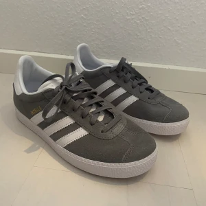 Nya Adidas Originals Gazelle storlek 36 2/3 gråa - Färg: Grå (Grey Three-Cloud White-Gold Metallic) Storlek: 36 2/3 Nya och oanvända. Tyvärr hann jag ta bort tags/lappar och slänga kartongen då tanken var att börja använda dom men det blev inte så pga har många skor. Populära och slutsålda. 