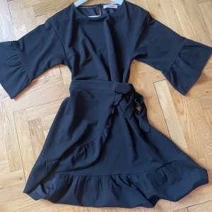 Svart miniklänning  - Svart midiklänning med volanger och knytning i midjan från co’couture. Tjockt, lyxigt tyg. 