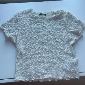 En vit croppad topp med ”skrynkligt” material från Gina tricot