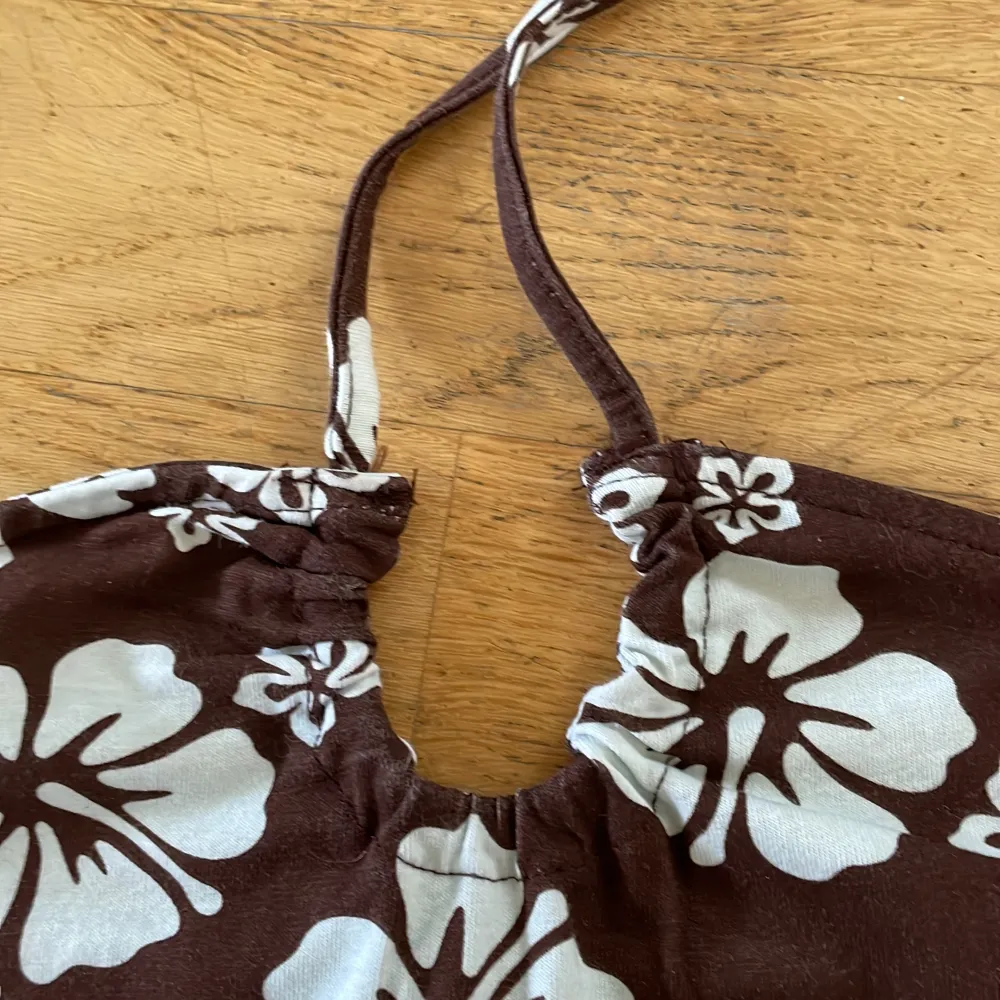 Fin sommrig klänning. Trikå. Det sitter snören på framsidan som man knyter i nacken. Den är brun med vita hawaii blommor.. Klänningar.