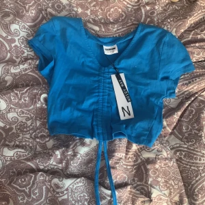 Kortärmad blå topp som har knyt band nere! - Helt ny! Lapp kvar! Helt oanvänd 