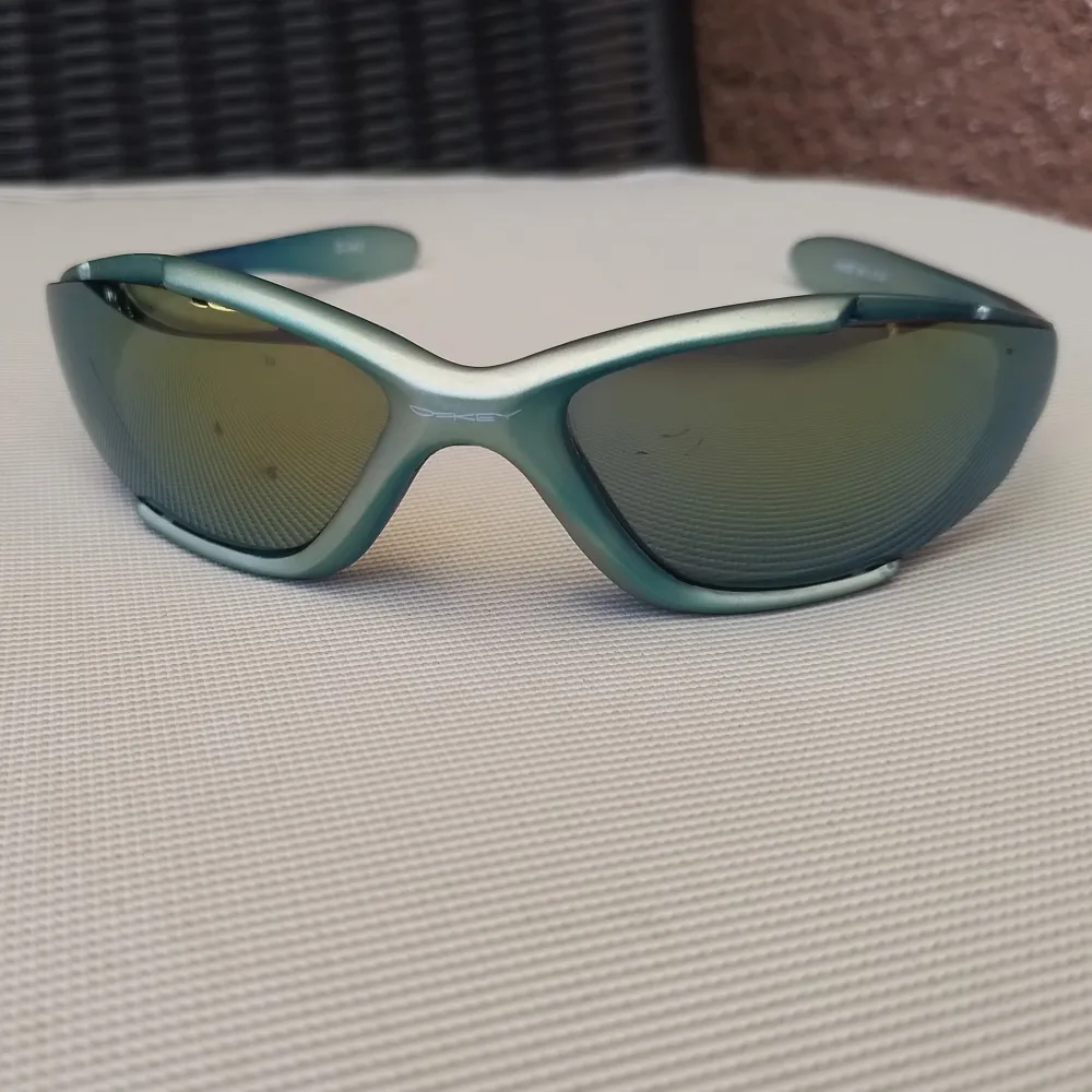 Ett par turkos/blå-grönmetallic solglasögon från Oakley. Glasen är utbytbara. Spegelglasen har några små nagg som inte märks när man bär dem (därav priset). Sjukt grymma solglasögon . Accessoarer.
