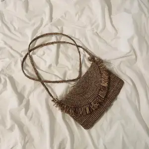 Unik liten axelremsväska i Raffia Crochet av mycket god kvalitet. Väskan har ett långt band och fransar. Från märket l’Atelier du Crochet. Storlek: 16 x 25 cm  Skickar snarast efter köp! Köparen står för frakten.