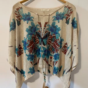 qed London beige mönstrad topp, storlek L - Snygg topp med ett vackert mönster av blommor och fjärilar. Toppen har en lös passform och en spännande design med en snodd i halsen och en frans i botten.  Skick: Mycket bra Längd: 53cm