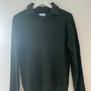 Mörkgrå tröja med krage - En mörkgrå tröja med krage och långa ärmar. Tröjan har en enkel design och är tillverkad i merino ull. Tröjan är något liten i storleken. 