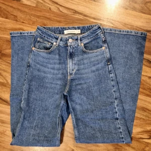 Blå jeans från Carin Wester - Ett par blå jeans från Carin Wester i storlek 34. Byxorna har en klassisk design med hög midja och en vid design från låren nedåt. De är högmidjade och har en rak passform. OANVÄND