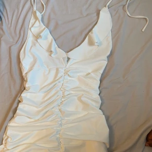 Vit klänning - Vit klänning med räfflade detaljer på nedre del med  volang aktiga kanter. 