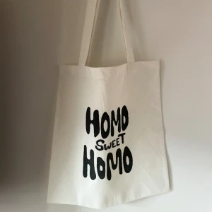 Tygkasse, tygväska, tygpåse  - Handsydd tygkasse med motivet ”homo sweet homo”.   Tillverkad i 100% återvunna textilier. Motivet är handmålad med textilfärg.   Mått: 32x35 cm  Hämtas på Södermalm alternativt skickas med post. 
