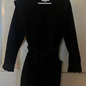 Kappa - Svart kappa med luva från Vila, används vi Max 5 tillfällen. Kappan kan stängas med både knapp och bälte 