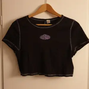 En svart croppad t-shirt med fina lila sömmar och lila tryck på  framsidan. Pris kan diskuteras.