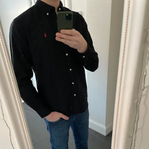 Ralph Lauren Skjorta - Säljer min svarta Ralph Lauren skjorta! Skjortan är i storlek L och modellen på bilden är ca 190cm och väger 80kg. Den är nästan helt ny och man ser inga tecken på att den är använd. Den klippta taggen finns och skickas med. Skriv för mer information!