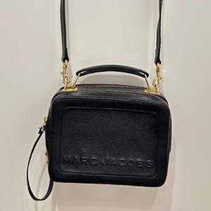 THE BOX 23 HAMMERED LEATHER BAG från Marc Jacobs i svart.  - äkta skinn - 17cm x 23cm x 8 cm - guldfärgade metalldetaljer   Väl använd, i gott skick utan några större skavanker, förutom att tyget iunti en av ”fickorna” av väskan är missfärgad. 
