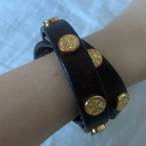 Tory burch armband - Fint mörkbrunt läderarmband från Tory Burch med guldiga nitar. Fint skick, lite slitet vid stängningen. Finns två lägen att stänga den på beroende på ens storlek💞 Skriv vid funderingar och kolla in mina andra annonser!