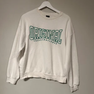 Collegetröja Ginatricot  - En vit collegetröja från Ginatricot i storlek S. Tröjan har grön broderad text framtill. Sitter normalt. 