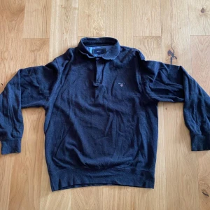 Mörkblå pikétröja från GANT - En mörkblå pikétröja från GANT i storlek XXL. Tröjan har långa ärmar och en klassisk krage med knappar. Den är tillverkad i ett mjukt och bekvämt material. Fett skön