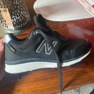 Svarta sneakers från New Balance - Ett par svarta sneakers från New Balance med vita sulor och snörning. Skorna har en bekväm passform och är designade för att ge bra stöd och komfort. De har en robust yttersula för bra grepp och hållbarhet. Använda en gång, tecken på användning men inga fel alls