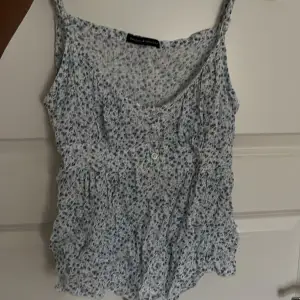 Säljer en söt blommig linnetopp från Brandy Melville. Toppen är vit med små blå blommor och har en v-ringad hals. Den är ärmlös och har knappar framtill. Perfekt för sommaren! superfint skick behöver bara strykas, den har även tunna band på baksidan så man kan knyta den❤️