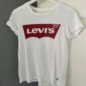 Säljer en vit t-shirt från Levi's med deras ikoniska röda logga på bröstet. T-shirten är i bomull och har korta ärmar. Perfekt för en casual look!