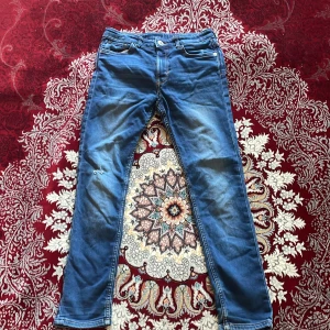 Blå skinny jeans - Säljer ett par blå skinny jeans i storlek 152. De är i denim och har en tight passform. Byxorna har några fläckar och är lite slitna, men de är fortfarande snygga och bekväma. Perfekta för vardagsbruk!!