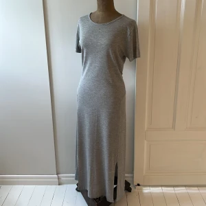 Grå lång trikåklänning från Filippa K - Säljer en superfin grå, lång trikåklänning från Filippa K. Den är gjord av mjuk och bekväm bomullstrikå, perfekt för både vardag och fest. Klänningen har korta ärmar och dubbla slitsar fram. Funkar året om beroende på hur man stylar 🩶