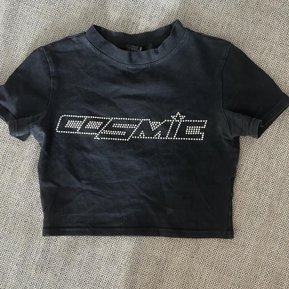 En svart croppad t-shirt med texten 'COSMIC' i rhinestones. T-shirten har korta ärmar och en rund halsringning💕. Toppar.