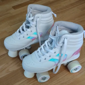 Vita rullskridskor med regnbågsdetaljer - Säljer ett par snygga vita rullskridskor från Decathlon i storlek 37. De har regnbågsfärgade detaljer på sidorna och är i nyskick. Perfekta för sommarens åkturer! De har snörning och är bekväma att ha på sig 🛼✨