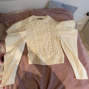 Beige stickad tröja med puffärmar - Säljer en superfin beige stickad tröja med unika puffärmar. Tröjan är i nyskick aldrig använd och perfekt för höst och vinter. Den har ett snyggt mönster på framsidan och är riktigt mysig att ha på sig. Passar perfekt till både vardag och fest!