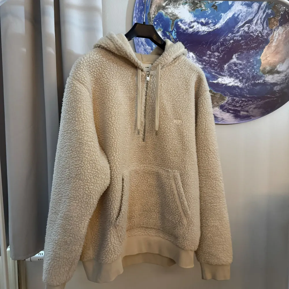 Säljer en supermysig beige fleece hoodie från Wood Wood. Den har en dragkedja framtill och en stor ficka på magen. Perfekt för kalla dagar när du vill vara varm och bekväm. Hoodien har en normal passform och är i nyskick. Perfekt för höst och vinter!. Hoodies.