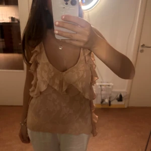 Beige blus med volanger - En elegant rosa blus med volanger framtill och på sidorna. Blusen är ärmlös och har en v-ringad halslinje, rätt så festlig och supergullig. Använd fåtal gånger