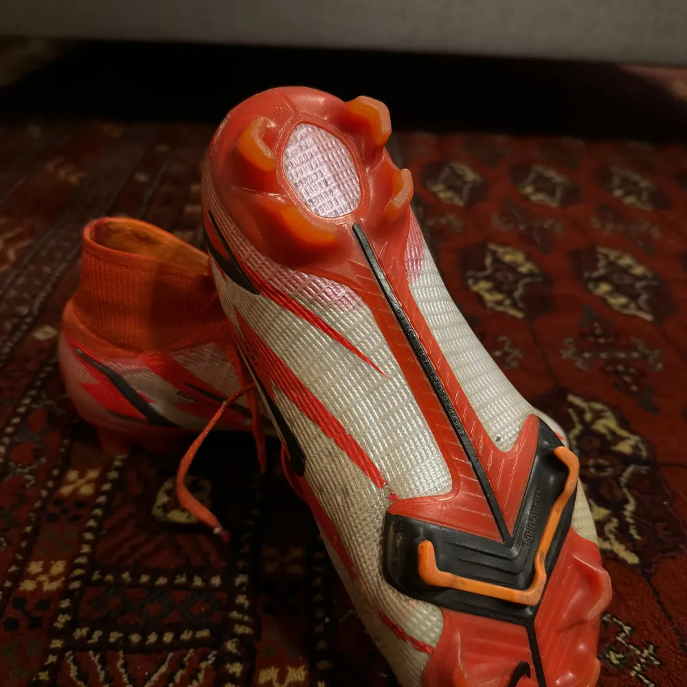 Säljer ett par Nike Mercurial fotbollsskor i nyskick. Skorna är i en cool orange och vit färgkombination med svarta detaljer och snörning. De har en tight passform och är perfekta för fotbollsträning och matcher. Sulan har en bra greppdesign för att ge bästa möjliga fäste på planen.. Skor.