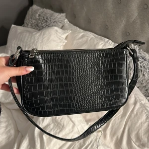 Svart axelväska med krokodilmönster - Säljer en snygg svart axelväska med krokodilmönster. Väskan är i skinn och har en dragkedja upptill. är rymlig🥰