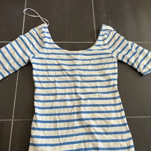 Randig klänning från Lindex - Säljer en superfin randig topp från Lindex i storlek XS. toppen är vit med blå ränder och har trekvartsärmar. Perfekt för sommaren.