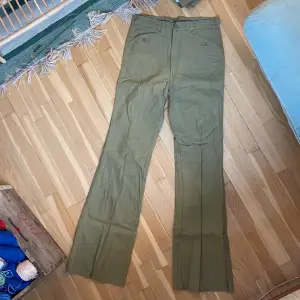 Vintage utsvängda byxor från Dobber, grönbeige färg. Helt nya, endast legat på lager.  Obs det är rålängd, de är alltså inte fållade utan bör sys upp i ens egen längd. Märkta size 31.  Mått cm: Midja: 37,5 Höft: 43,5 Ben: 86,5  