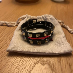 Valentino Garavani rockstud armband  - Säljer ett Valantino Garavani rockstud armband med dubbla band. Armbandet är i svart läder med guldiga detaljer. Det är använt ett fåtal gånger och är i gott skick. Armbandet är köpt på Valentino butiken på NK, Stockholm. Nypris är 3000 kr.  