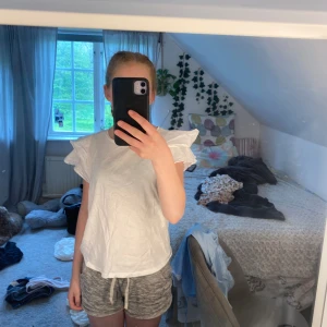 Vit T-shirt  - Vit t-shirt med volanger på sidan. Perfekt till sommaren! Str xs. 