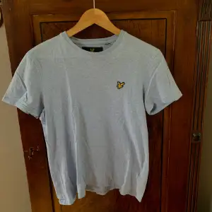 Ljusblå melerad T-shirt från Lyle & Scott med liten gul logga på vänster bröst. 100% bomull 