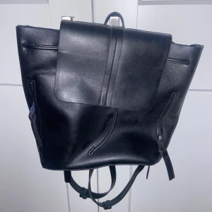 Svart ryggsäck - svart ryggsäck med en minimalistisk design. Väskan har en klaff med dragsko och justerbara axelremmar. aldrig använd. 