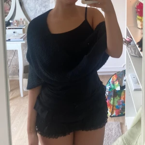 Svart stickad klänning - En svart stickad tub halsduk som är stretchig och stor. Den är tillverkad av ett stickat material som ger en texturerad känsla.