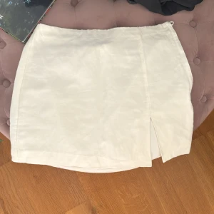 Vit linne minikjol - Säljer denna vita somriga linne kjol pga att den är tyvärr för liten för mig 😊den har en liten slits på vänster lår och har även dragkedja på sidan💕är högmidjad för folk som bär 36 men lågmidjad för XS