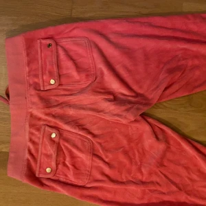 Juicy byxor - Säljer ett par juicy byxor i en gammal modell, men är så lyckligt lottad som äger ett par från för många år sedan! De är i en stark rosa färg, med fina guld knappar på bakfickorna. Rhinestonesen har gått av på juicy märker och det är defekten med byxorna.